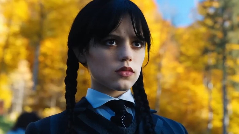 Wednesday Addams in front of fall foliage staring