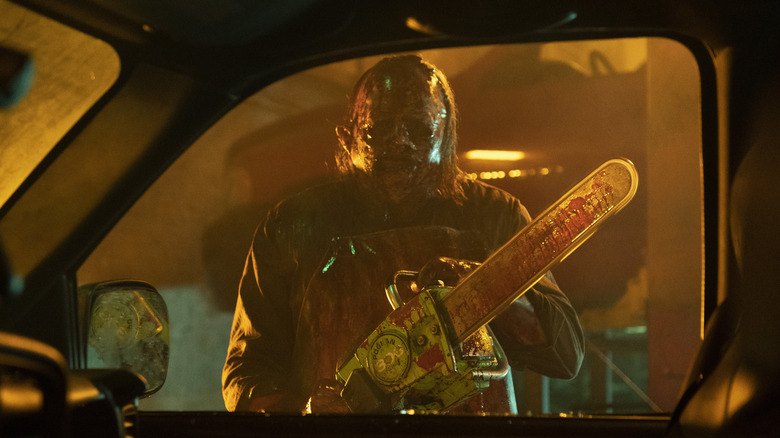 Leatherface holding a chainsaw and staring into a car window in Texas Chainsaw Massacre (2022)