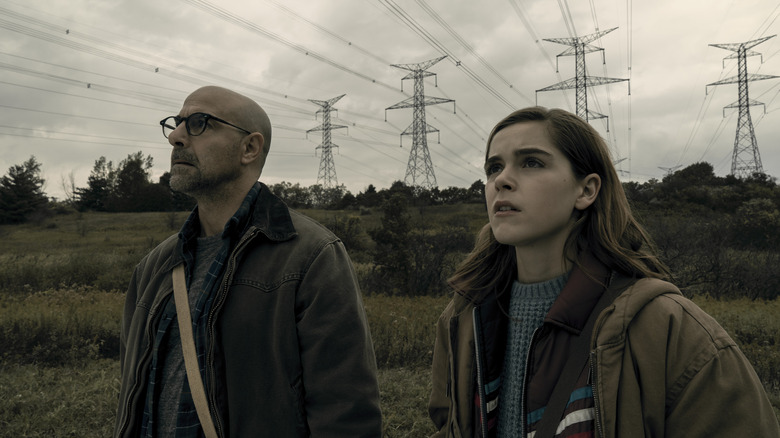 Stanley Tucci as Hugh stands next to Kiernan Shipka as Ally in a field in The Silence